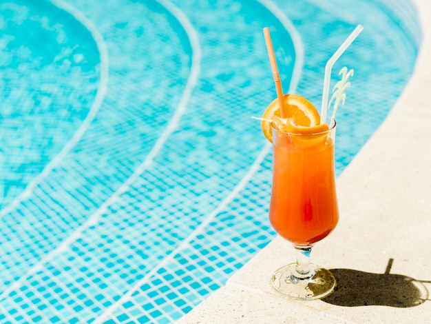 Cóctel con rodajas de naranja y pajitas colocadas en la piscina.