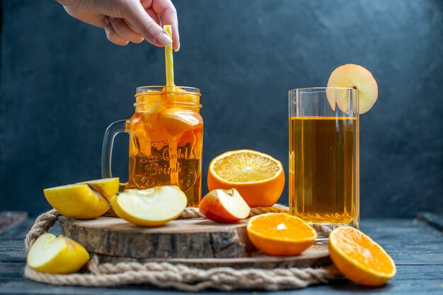 Cóctel de vista frontal cortadas naranjas y manzanas en tablero de madera en la oscuridad