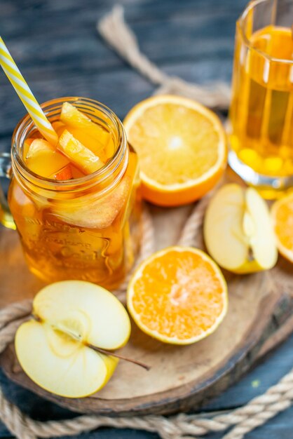 Cóctel de vista frontal cortadas naranjas y manzanas en tablero de madera en la oscuridad