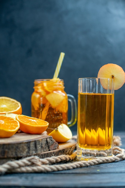 Cóctel de vista frontal cortadas naranjas y manzanas en tablero de madera en la oscuridad