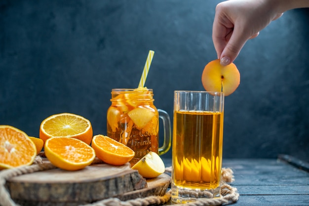 Cóctel de vista frontal cortadas naranjas y manzanas en tablero de madera en la oscuridad