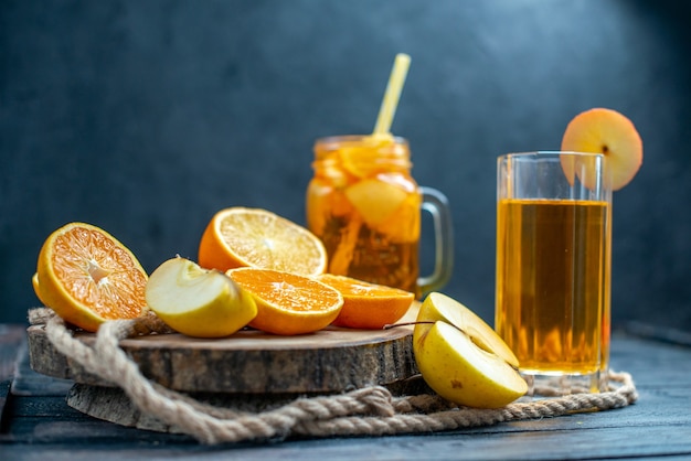 Cóctel de vista frontal cortadas naranjas y manzanas en tablero de madera en la oscuridad