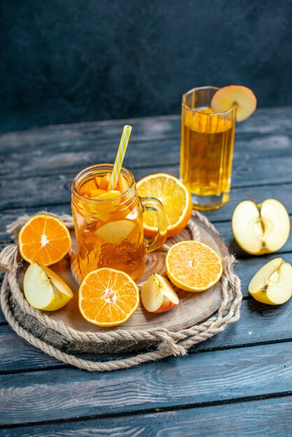 Cóctel de vista frontal cortadas naranjas y manzanas en tablero de madera en la oscuridad