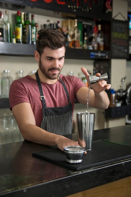 Coctelera de colada masculina hermosa del barman en coctelera en la barra mostrador
