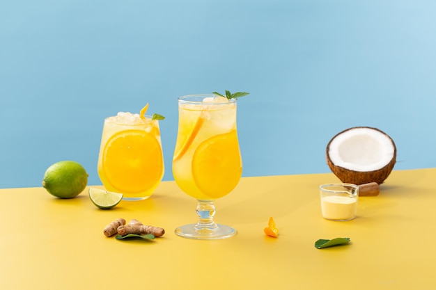 Cócteles frescos con naranja, menta, lima, jengibre y coco sobre un fondo amarillo y azul