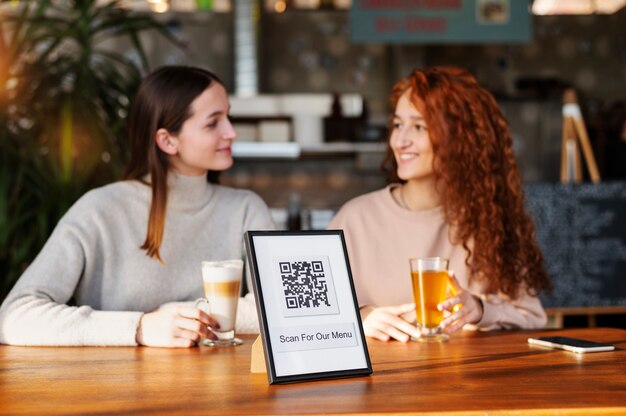 Código qr en la mesa con dos amigos disfrutando de bebidas