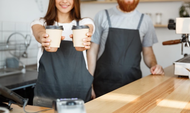 Coffee Business Concept Un joven barbudo positivo y una hermosa y atractiva pareja de baristas dando una taza de café para llevar a la clientela en la cafetería moderna