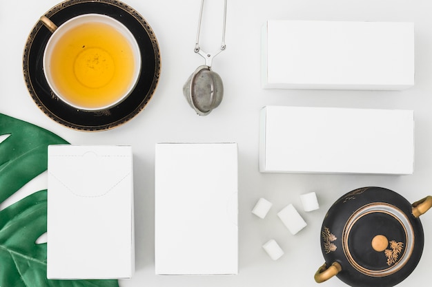 Colador de té y cajas blancas con terrones de azúcar sobre fondo blanco