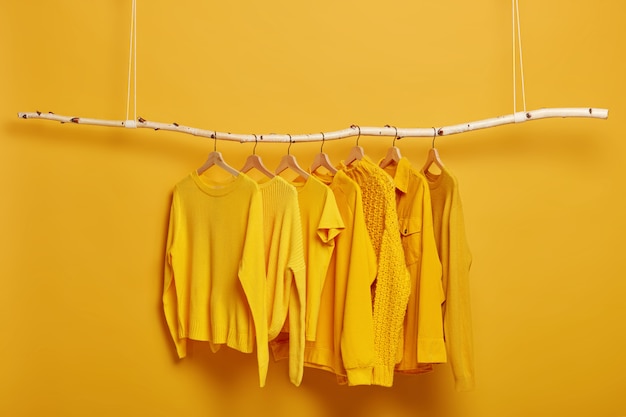 Colección de jerséis y chaquetas de color amarillo liso para mujer colgadas en perchero en vestidor. Enfoque selectivo. Ropa de moda de invierno u otoño.