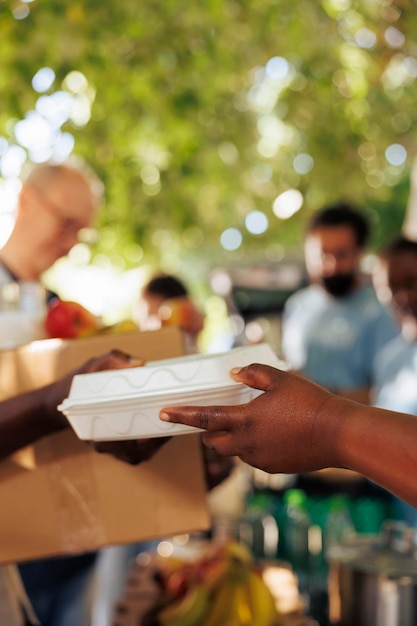 En una colecta de alimentos, un voluntario de etnia afroamericana le sirve una comida caliente a una persona pobre y hambrienta. Primer plano de una persona necesitada menos privilegiada que recibe comida gratis de un trabajador de caridad.