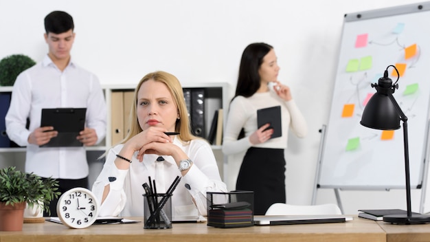 Colega de pie detrás de la seria joven empresaria en el lugar de trabajo