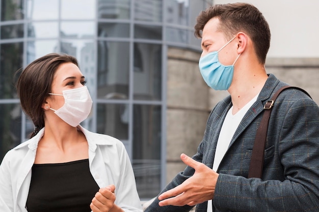 Colegas al aire libre durante la pandemia charlando con máscaras faciales