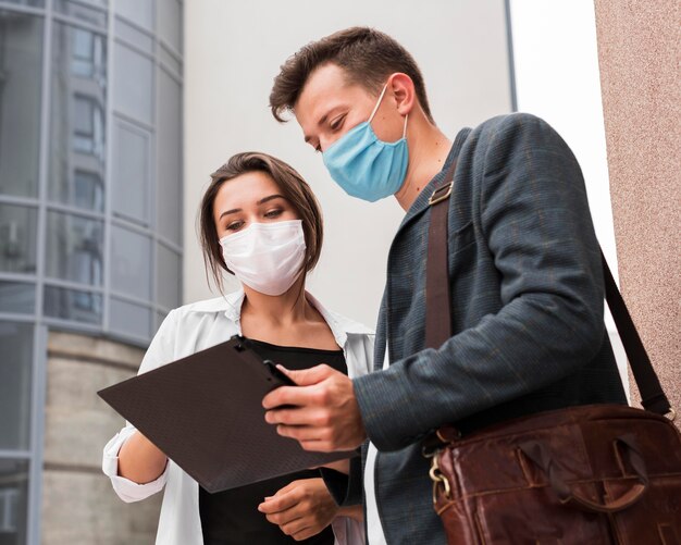 Colegas al aire libre durante la pandemia mirando el bloc de notas con máscaras faciales