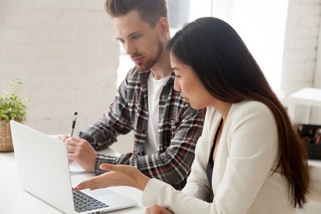 Colegas asiáticos y caucásicos trabajando juntos discutiendo tareas con laptop