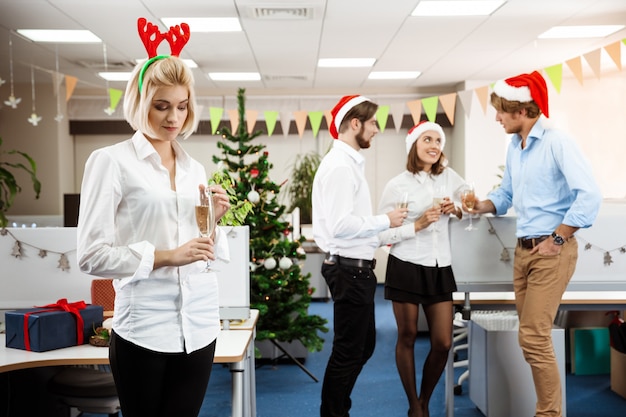 Colegas celebrando la fiesta de Navidad en la oficina bebiendo champán sonriendo.