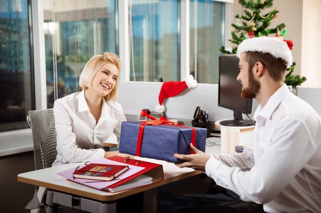 Colegas celebrando la fiesta de Navidad en la oficina sonriendo dando regalos.