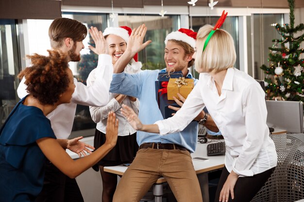 Colegas celebrando la fiesta de Navidad en la oficina sonriendo dando regalos.