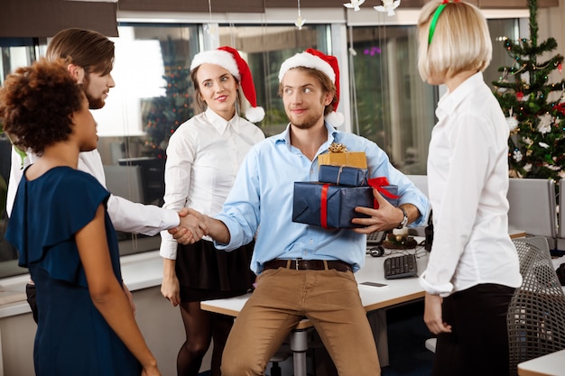 Foto gratuita colegas celebrando la fiesta de navidad en la oficina sonriendo dando regalos.