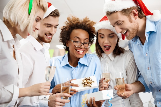 Colegas celebrando la fiesta de Navidad en la oficina sonriendo dando regalos.