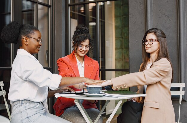 Colegas discutiendo datos en el café al aire libre. Mujeres multirraciales que analizan la estrategia productiva para la proyección empresarial utilizando documentos en street cafe