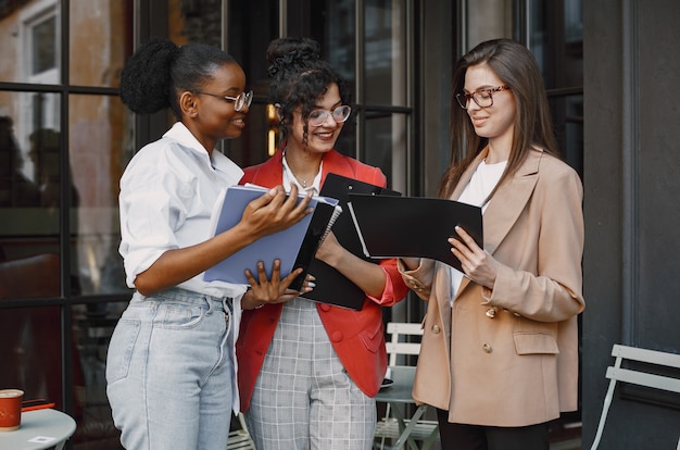 Colegas discutiendo datos en el café al aire libre. Mujeres multirraciales que analizan la estrategia productiva para la proyección empresarial utilizando documentos en street cafe