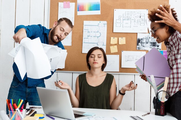 Colegas discutiendo, discutiendo dibujos, nuevas ideas mientras una mujer medita