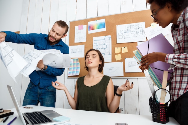 Colegas discutiendo, discutiendo dibujos, nuevas ideas mientras una mujer medita