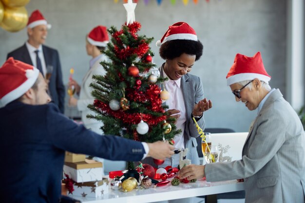 Colegas felices decorando el árbol de Navidad en una fiesta en la oficina