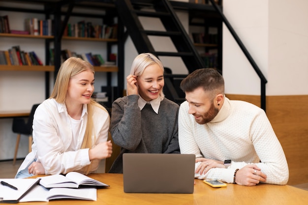 Colegas hablando y estudiando en una biblioteca usando una computadora portátil