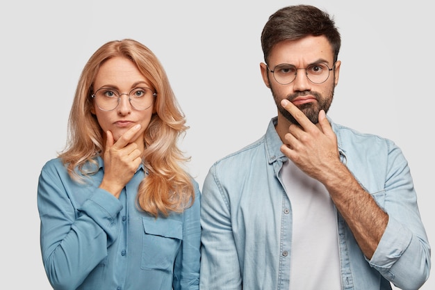 Foto gratuita los colegas de hombre y mujer reflexivos sostienen la barbilla y se concentran en resolver el problema, miran directamente