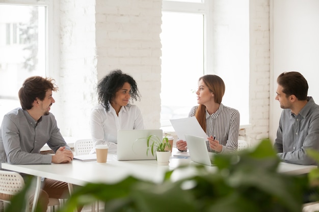 Colegas multirraciales masculinos y femeninos discutiendo en la reunión del equipo