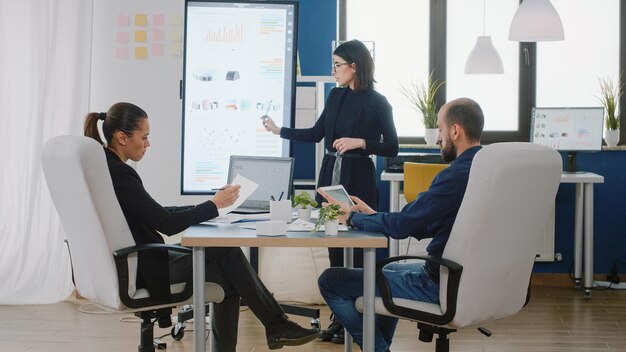 Colegas que asisten a una reunión de negocios en la sala de juntas para la planificación de proyectos y la estrategia de marketing. Personas que trabajan con gráficos en televisión y dispositivos para gestión y presentación.