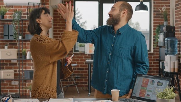 Colegas que chocan los cinco mientras intercambian ideas para diseñar proyectos y planificar la estrategia de marketing. Hombre y mujer celebrando el éxito en la reunión de investigación, mostrando unidad en la oficina de inicio.