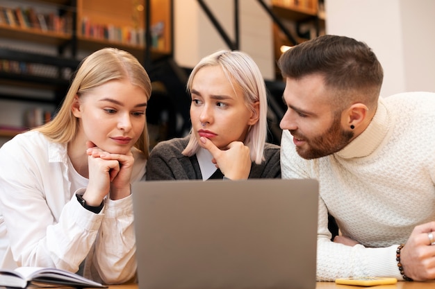 Colegas que estudian en una biblioteca usando una computadora portátil