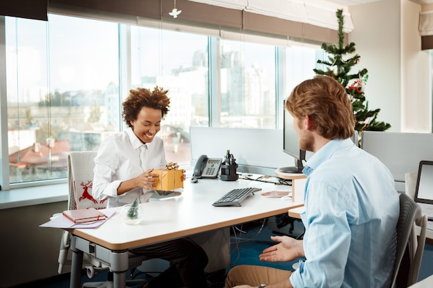 Colegas que trabajan en la oficina el día de Navidad dando regalos.