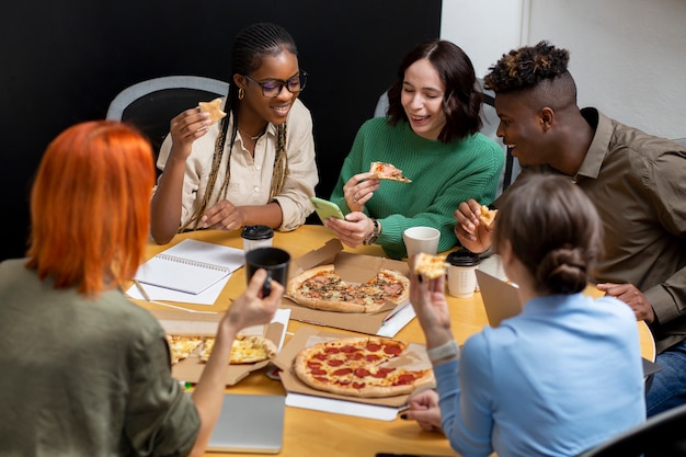 Colegas sonrientes comiendo pizza en el trabajo plano medio