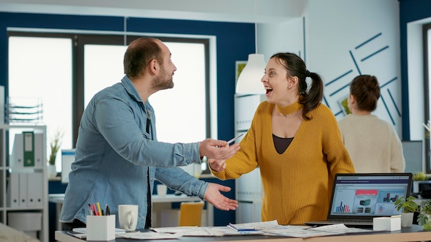 Foto gratuita colegas sonrientes en la oficina de inicio haciendo un gesto de cinco manos celebrando el éxito empresarial de pie en el escritorio. compañeros de trabajo felices disfrutando de buenos resultados del trabajo en equipo mirando portátiles con gráficos.