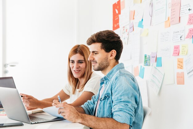 Colegas sonrientes que miran el ordenador portátil en el lugar de trabajo