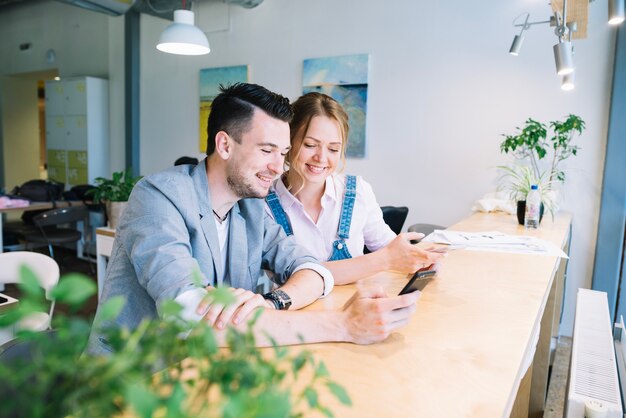 Colegas sonrientes que usan teléfonos inteligentes en la oficina