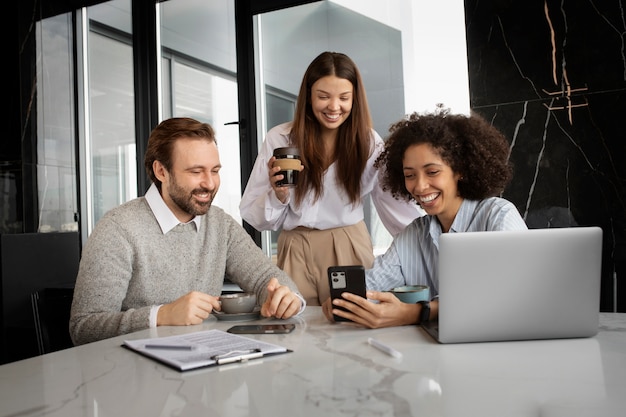 Colegas sonrientes de tiro medio con teléfono inteligente