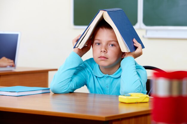 Colegial sujetando un libro encima de su cabeza