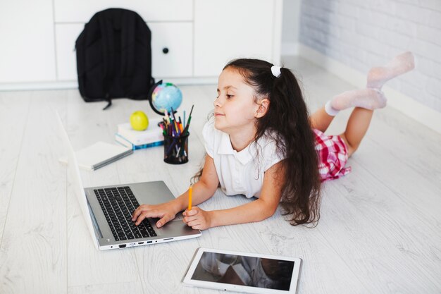 Colegiala acostado y usando la computadora portátil