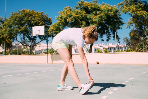 Colegiala adolescente estirando las piernas en el campo de deportes
