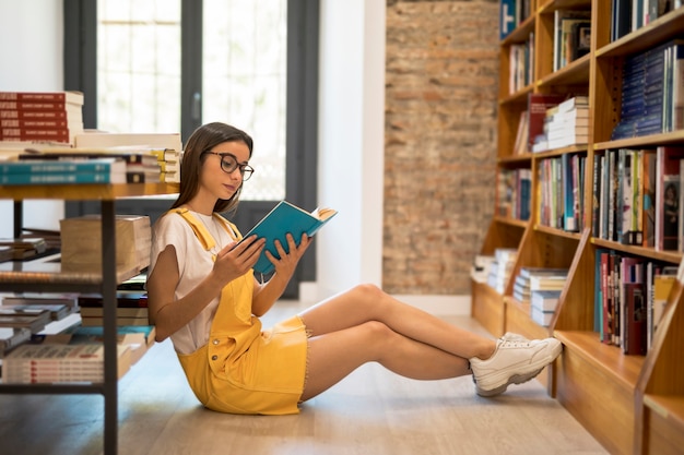 Colegiala adolescente con libro en piso.