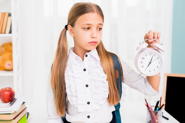 Foto gratuita colegiala cansada con mochila con reloj en el aula