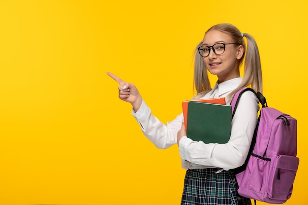 Colegiala feliz del día mundial del libro con gafas y mochila rosa mirando a la izquierda