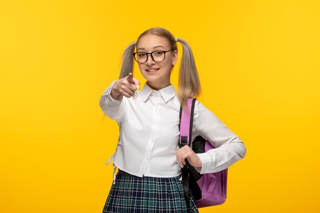 Colegiala feliz del día mundial del libro en linda falda uniforme a cuadros con mochila rosa