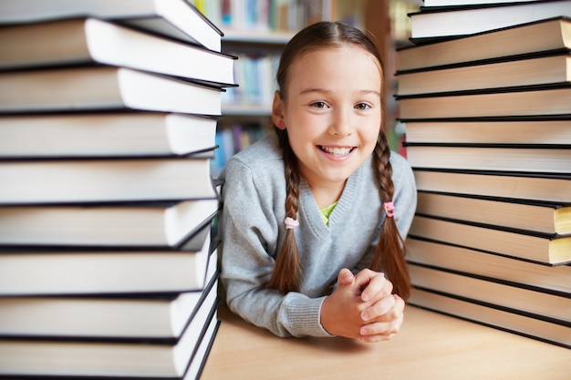 Colegiala feliz rodeada de pilas de libros