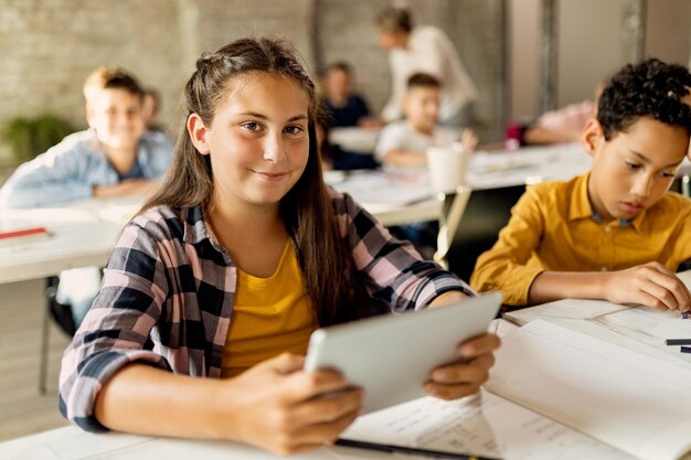 Colegiala feliz usando tableta digital durante una clase en el aula