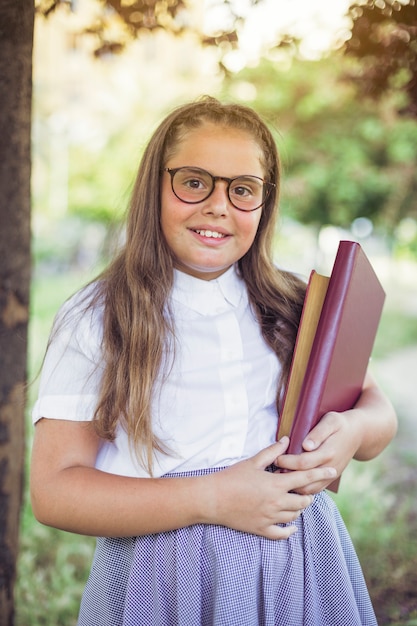 Colegiala en gafas de pie en el parque con libros